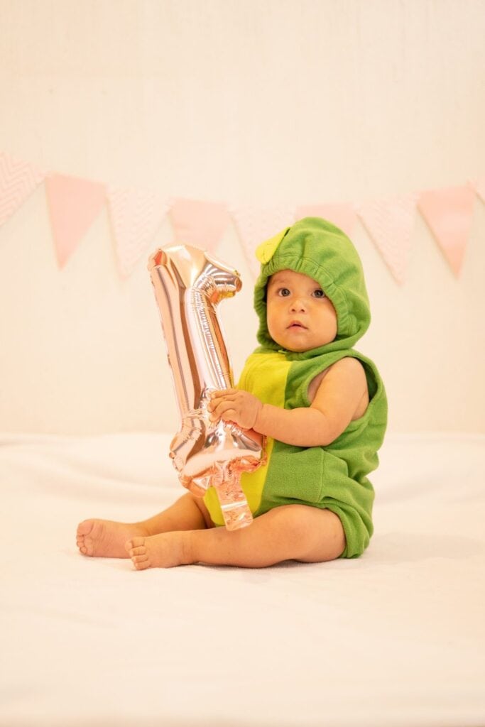 A baby in a green romper holding an inflatable balloon